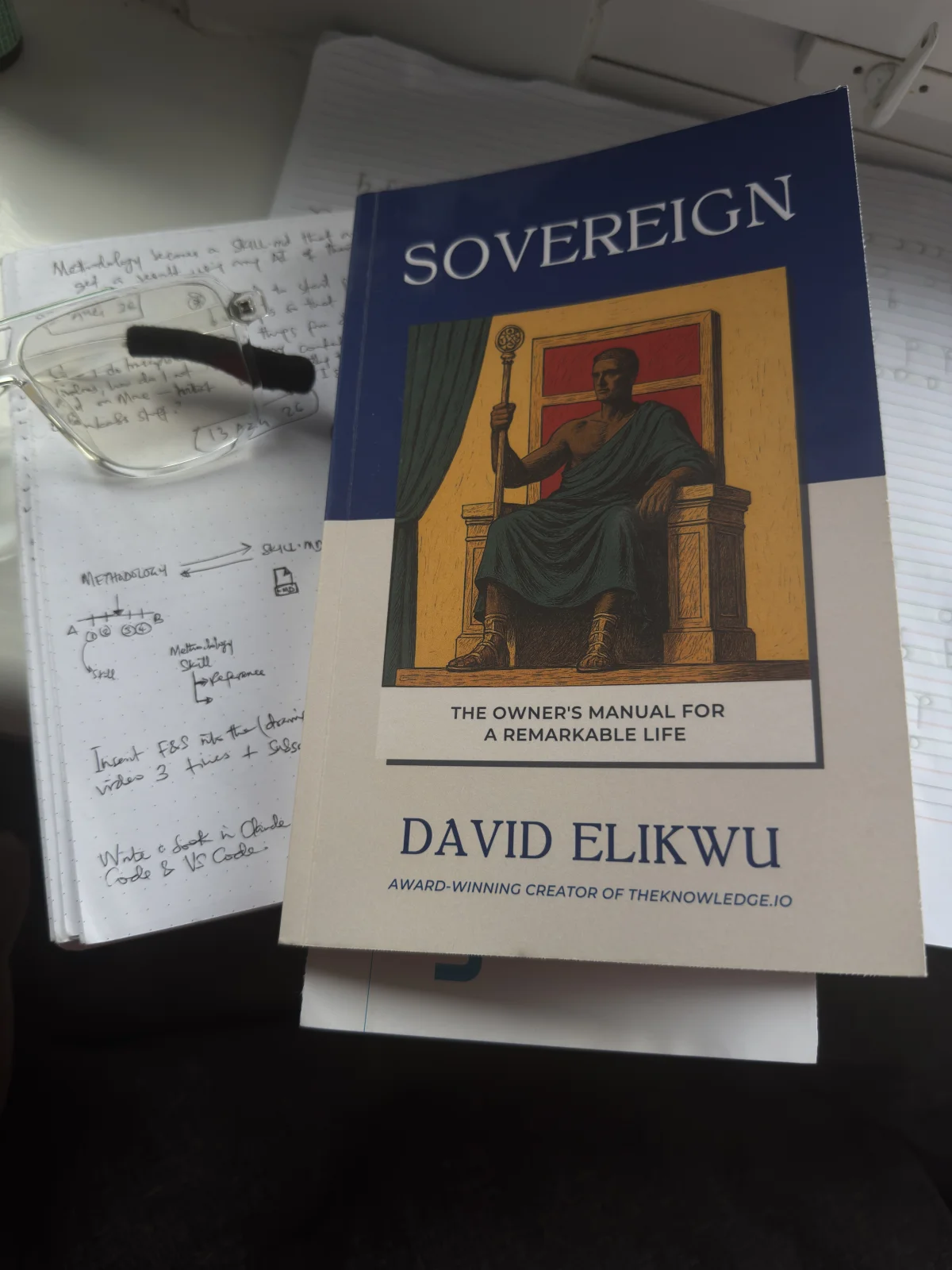 Sovereign by David Elikwu resting on Dayo's own handwritten notebook, open to process notes on methodology and skills